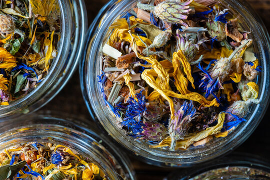 Dry flower and herbal tea leaves in a glass jar on wooden background. Herbal collection of chamomile, cornflower, mint, sea buckthorn, lemongrass, wild rose, dried citrus fruits and apple