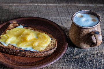 Bread toast with butter, honey on plate and cappuccino coffee in a clay cup on wooden table, closeup