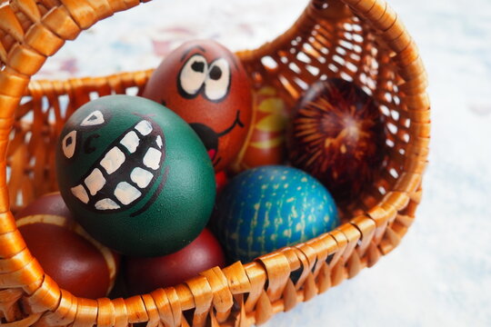 Easter eggs painted in different colors with painted laughing faces. Funny grimaces with eyes, tongue and big white teeth. Scary face for Halloween. Emoticon for Easter Wicker basket. White