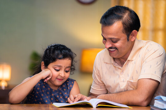 focus on father, Father helping his daughter for reading book at home during evening - concept of education, caring family and responsibility