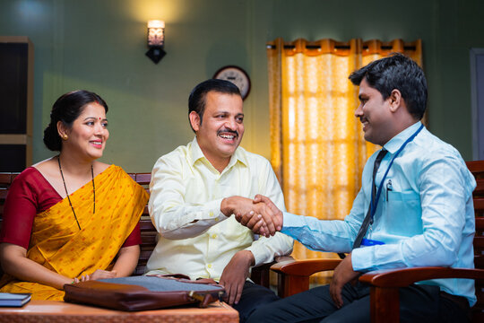 Banking officer greeting by shaking hand to couple by explaining about insurance at home - concept of financial adviser, doorstep service or support and investment planning