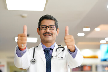 Indian male doctor showing thumps up at hospital.