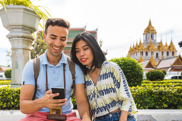 Happy multiracial couple or friends in Bangkok checking on the phone