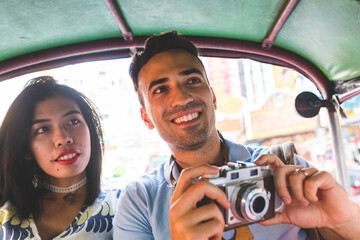 Happy multiracial couple or friends on a tuk tuk exploring Bangkok and taking photos