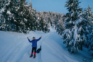 Man in snowshoes is standing, holding drone controller. In the majestic forest of Carpathian mountains