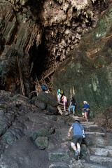 Local tour guide with traditional lantern guiding tourists through the tall and dark chambers of Tham Nam Lod caves