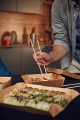 Using chopsticks. Man in casual clothes is with sushi that is in the paper eco box