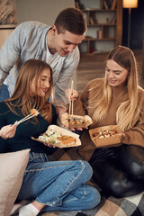 Man with women. Friends are sitting indoors at home and eating sushi together