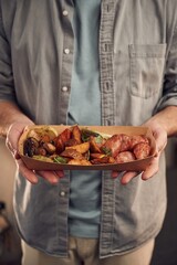 Close up view. Man in casual clothes is holding food that are in the paper eco box. Potatoes, sausages, mushrooms, zucchini
