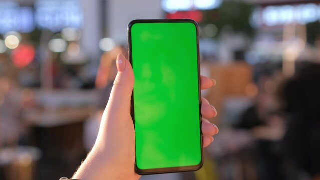 Mall.Use green screen for copy space closeup. Chroma key mock-up on smartphone in hand. Woman holds mobile phone and looking photos or pictures