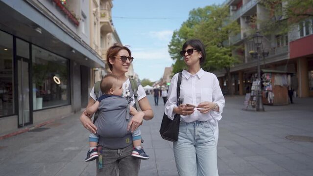 Two young women are walking in the city street with baby. The concept of family and healthy lifestyle. Mother whit baby