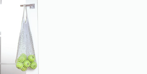 Green fresh apples in a net hang on a white door handle. the concept of freshness naturalness vitamins veganism