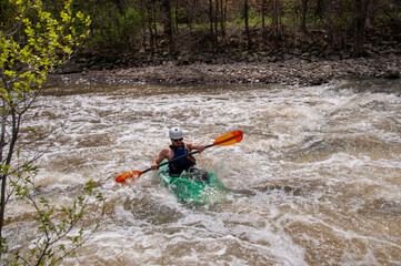 A man white water kayaks on a small river