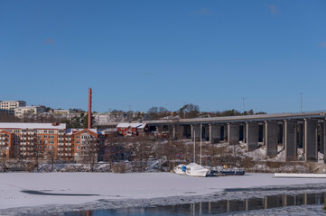 Fototapeta na wymiar Moored boats in the frozen bay Bällstaviken under the bridge Västerbron and waterfront apartment buildings, a snowy sunny spring day in Stockholm
