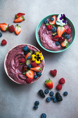 Two summer acai smoothie bowls with strawberries, blueberries,   on gray concrete background....