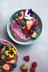 Two summer acai smoothie bowls with strawberries, blueberries,   on gray concrete background. Breakfast bowl with fruit and cereal, close-up, top view, healthy food