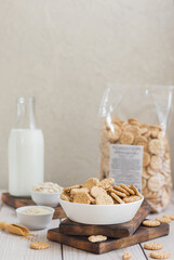 Small round crackers with oatmeal and sesame seeds in a white ceramic bowl on a wooden board on the table.. in the background is a bottle of milk and a package of crackers.