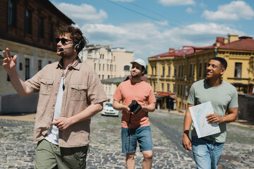 smiling multicultural tourists with travel map and vintage camera walking with guide in headset on historical district in Kyiv.