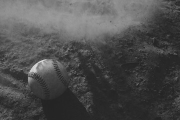 Baseball game concept during summer sports season with dirt in motion over ball on field in black and white, copy space on background.