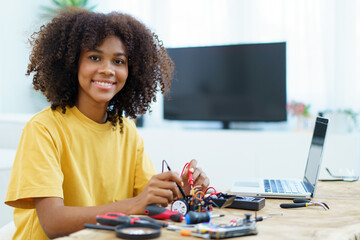 Happy cheerful American - African black ethnicity female university student learning about robotic and programing by herself, woman assemble a robot.