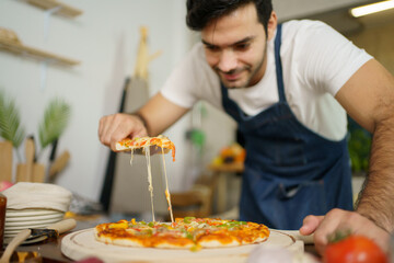 Professional Italian chef baking a cheesy Hawaiian pizza at home. Chef cutting a pizza portion and picking up.