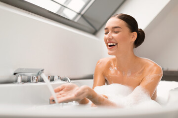 Obraz na płótnie Canvas Woman Taking Bath Touching Running Water From Tap In Bathroom