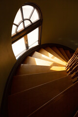 Vertical high angle view of wooden spiral staircase in old building, with sun streaming from an arched window