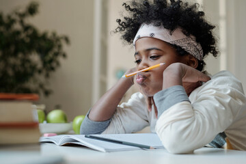Fototapeta Distracted and lazy schoolboy reluctant to do homework sitting by desk with open copybook and holding pencil between nose and upper lip obraz