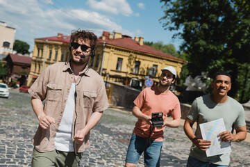 positive multiethnic tourists with vintage camera and map smiling during excursion with tour guide...