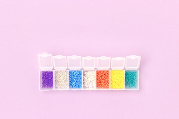 Multicolored beads in a storage container on a purple background.