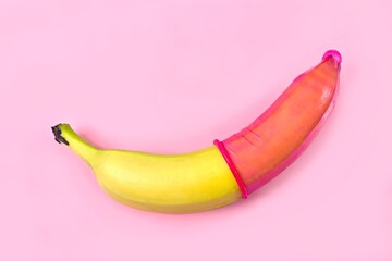 Red condom on banana with pink background. Safe sex concept.  - obrazy, fototapety, plakaty