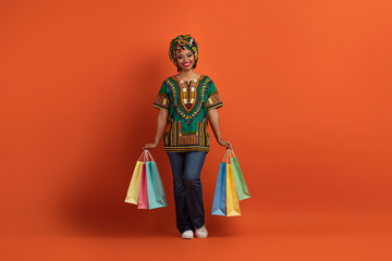 Fototapeta premium Happy black lady in african costume posing with her purchases