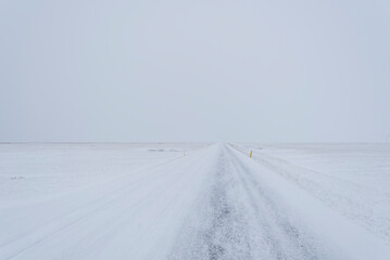 Straight icy road on a remote location in Iceland during winter with almost no difference between the snowy land and sky.