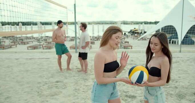Group of young joyful friends playing volleyball on the sandy beach