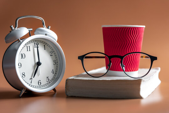 Alarm clock, cup of coffee, glasses and book, morning concept.