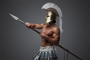 Studio shot of strong greek man with plumed helmet and spear against gray background.