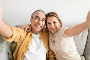 Love lives forever. Happy senior spouses taking selfie, enjoying spending time together while sitting on sofa