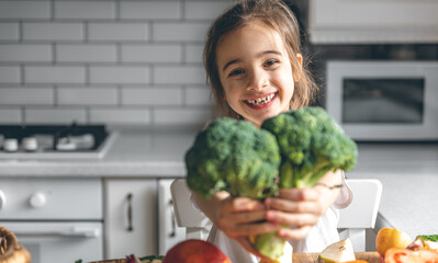 Funny little girl with broccoli in the kitchen.
