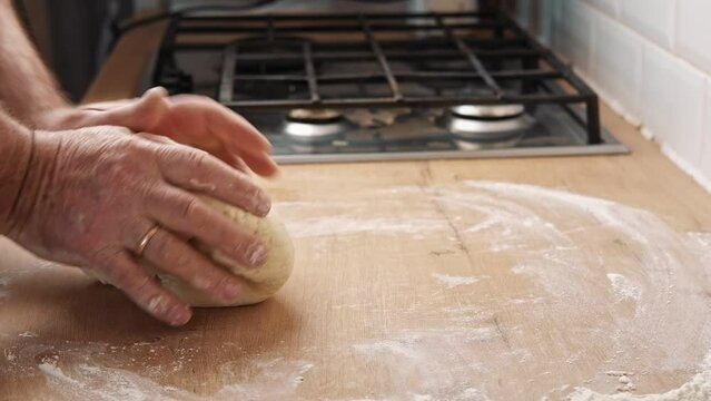 Male hands kneading dough, baking preparation closeup. Pastry Man kneads making yeast dough for pizza, burger, buns, muffins or pie. Anonymous baker. Bakery chef cooking bake in a kitchen professional