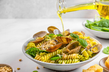 Pouring olive oil in seafood pasta with clams vongole, parmesan cheese, spinach, pine nuts. Italian...