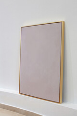 Gold colored metal frame propped up on a white wall.
