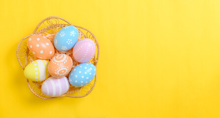Fototapeta na wymiar Happy easter celebration holiday. colourful pastel painted eggs in wicker basket nest decoration on a yellow background. Seasonal greeting gift card concept. Top view, flat lay, copy space.