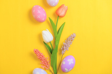 Fototapeta na wymiar Happy Easter holiday greeting card design concept. Colorful Easter Eggs and spring flowers on yellow background. Flat lay, top view, copy space.