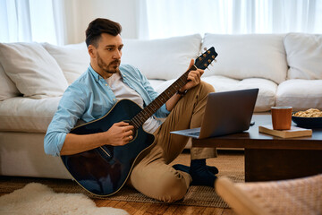 Mid adult man plays acoustic guitar while watching online tutorial on laptop.