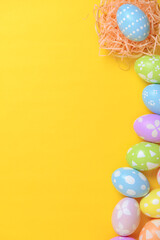 Happy easter celebration holiday. colourful pastel painted eggs in wicker basket nest decoration on a yellow background. Seasonal greeting gift card concept. Top view, flat lay, copy space.