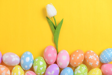 Happy Easter holiday greeting card design concept. Colorful Easter Eggs and spring flowers on yellow background. Flat lay, top view, copy space.
