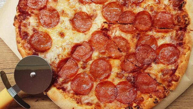 Top view of a delicious pepperoni pizza with a round cutter knife on the wooden table in the kitchen.