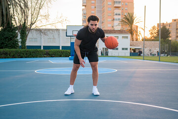 Fototapeta premium Afro Latin man playing basketball, bouncing the ball, on a court at sunset
