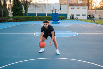 Fototapeta premium Afro Latin man playing basketball, bouncing the ball, on a court at sunset