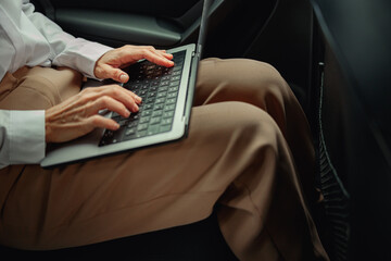 Close up of woman sales manager working on laptop sitting car backseat on the way to office